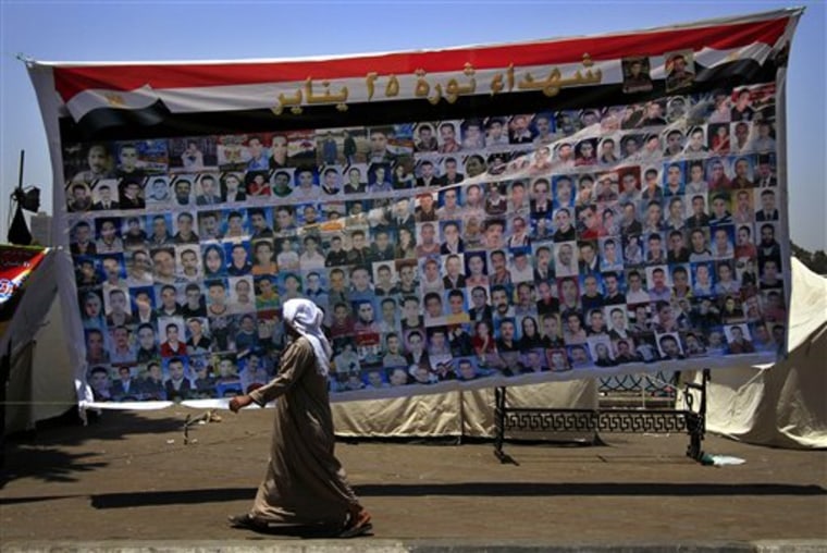 An Egyptian man passes by a banner picturing people killed by Egyptian security forces during the revolution, with Arabic words on top that read, \" the martyrs of 25th of Jan. revolution, \" as members of the victims' families hold a protest calling for the speedy trial of former President Hosni Mubarak and former interior minister Habib el-Adly in front of the National TV building in Cairo, Egypt, Sunday, June 26, 2011. (AP Photo/Khalil Hamra)